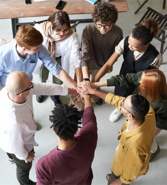 Menschen im Kreis stehend, Hände in der Mitte übereinander legend, symbolisieren Zusammenarbeit und Teamwork